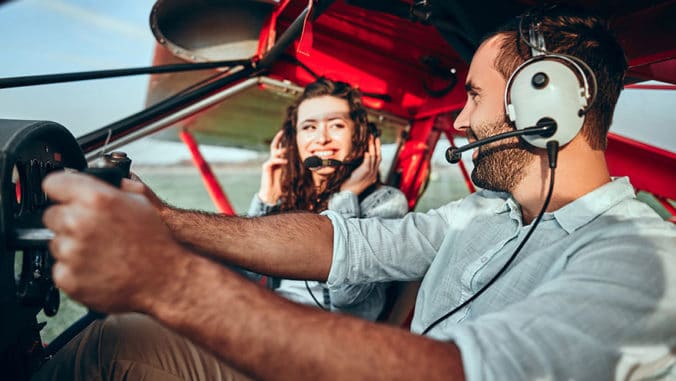 Cool young pilot and happy young woman sitting in cabin of private airplane.